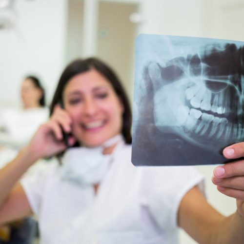 Dentist checking a x-ray report while talking on mobile phone at aesthetic clinic